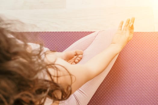 Young woman with long hair in white swimsuit and boho style braclets practicing outdoors on yoga mat by the sea on a sunset. Women's yoga fitness routine. Healthy lifestyle, harmony and meditation