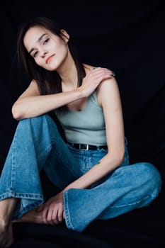 woman in denim pants sits on a chair on a black background