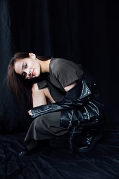 woman in a leather jacket sits on a black background