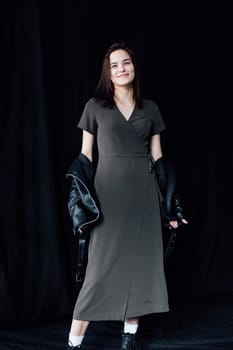 woman in a leather jacket stands on a black background