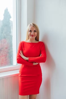 a woman in red dress stands in a room by the window