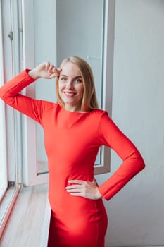 a woman in red dress stands in a room by the window