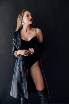 woman in a leather cloak and black clothes stands on a black background
