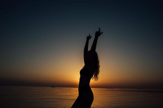 silhouette of woman in a swimsuit on the beach at sunset by the sea walk rest
