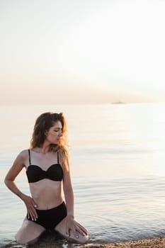 a woman in black swimsuit sitting in the water in the sea relaxing on the beach