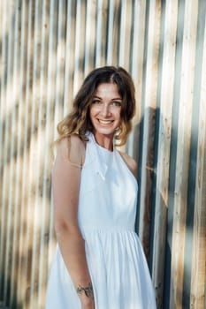 woman in a white dress stands against a wooden wall in a park on the street walk