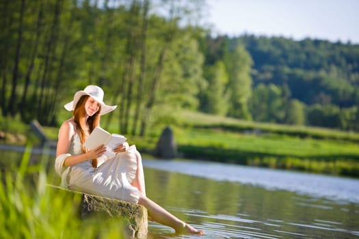 Long red hair romantic woman relax by lake with book