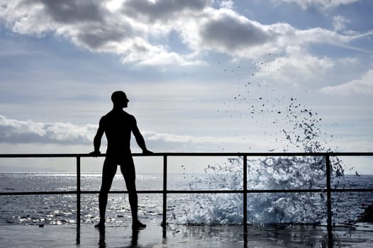 Silhouette of young man standing at the seaside, wave splash