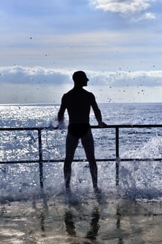 Silhouette of young man standing at the seaside, wave splash