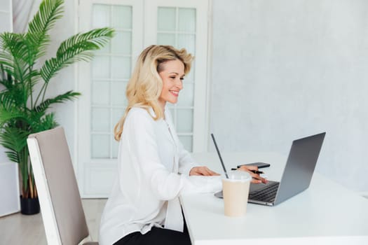 a woman in the office with a laptop computer records in a notebook remote work conversation on skype internet online communication