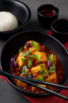Mapo Tofu bowl with side sauces on black stone table
