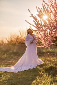 Woman blooming peach orchard. Against the backdrop of a picturesque peach orchard, a woman in a long white dress enjoys a peaceful walk in the park, surrounded by the beauty of nature