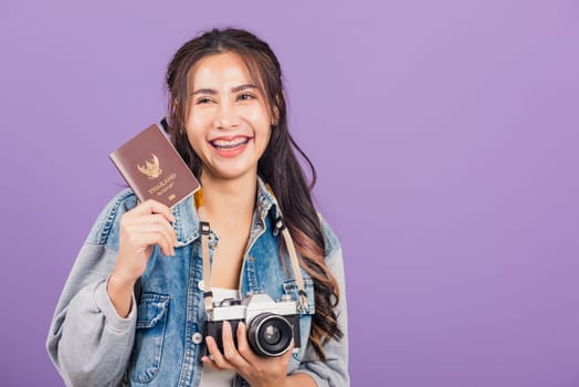 Happy Asian portrait beautiful young woman excited smiling in summer vacation holding passport and vintage photo camera, Thai female ready travel trip looking at camera isolated on purple background