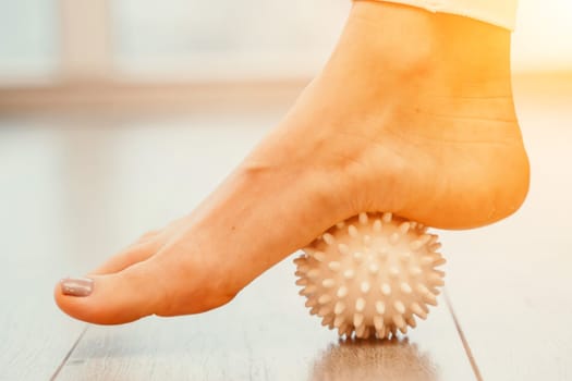 Athletic slim caucasian woman doing thigh self-massage with a massage ball indoors. Self-isolating massage.