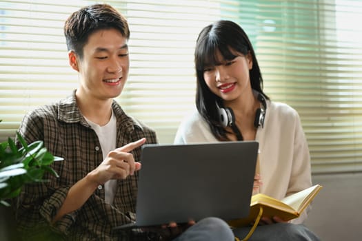 Smiling asian male student doing group project with his classmate on laptop. Education and youth lifestyle concept.