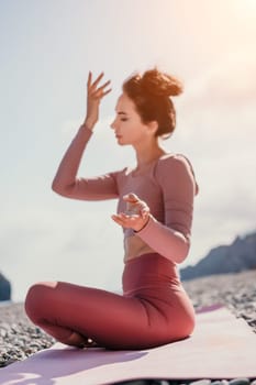 Young woman with long hair in white swimsuit and boho style braclets practicing outdoors on yoga mat by the sea on a sunset. Women's yoga fitness routine. Healthy lifestyle, harmony and meditation