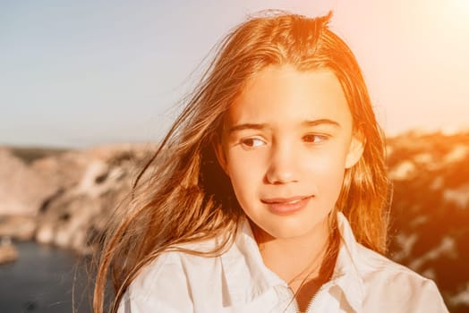 Brown-haired young romantic teenager girl corrects long hair on beach at summer evening wind