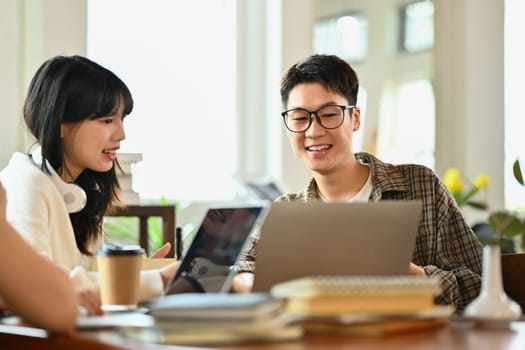 Friendly asian man student doing group project or preparing presentation on laptop with classmates.