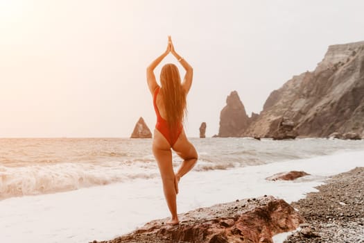 Woman sea yoga. Back view of free calm happy satisfied woman with long hair standing on top rock with yoga position against of sky by the sea. Healthy lifestyle outdoors in nature, fitness concept