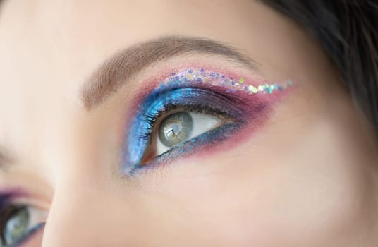 Close-up of colourful glitter and eyeshadows, festive bright eye makeup on girls face. Cat eye technique and colourful mix of shades. Mua, creative concept