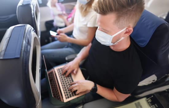 Top view of man work in air, open laptop device, facemask protection, busy freelancer on flight. Typing mail, prevent infection, passenger. Trip concept