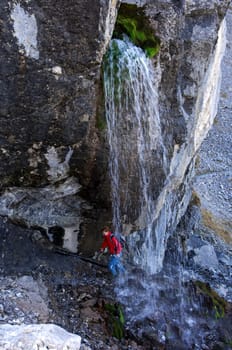 Hiker crosses a refreshing waterfall,Alps