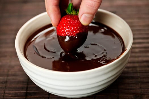 Hand dipping strawberry in chocolate