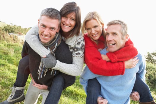 Two Couples Having Piggyback Ride In Autumn Landscape
