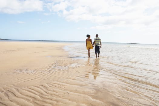 Romantic Young Couple Walking Along Shoreline Of Beach Holding Hands
