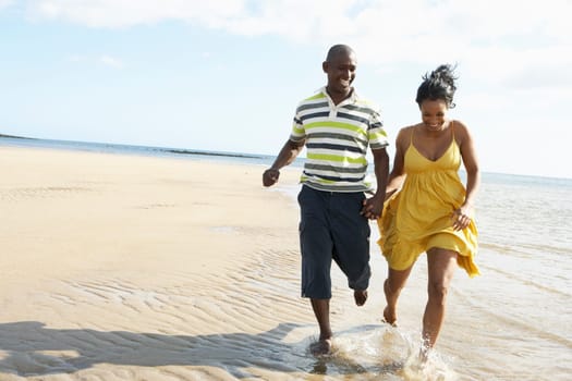 Romantic Young Couple Running Along Shoreline Of Beach Holding Hands