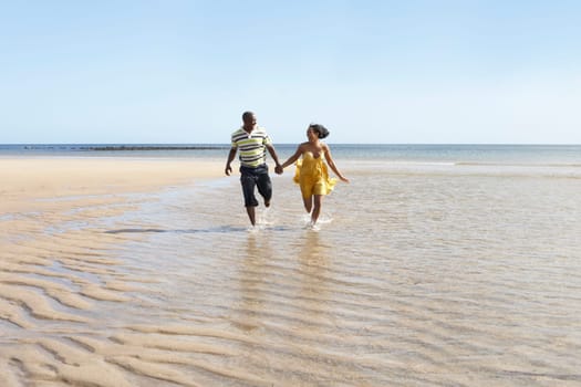 Romantic Young Couple Running Along Shoreline Of Beach Holding Hands