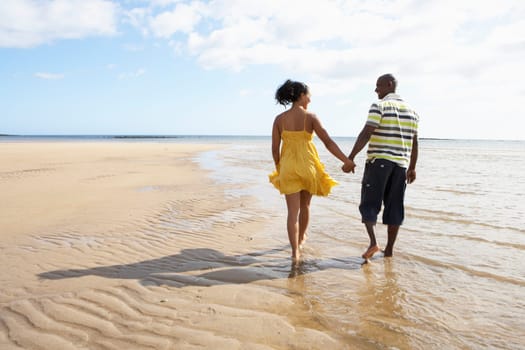 Romantic Young Couple Walking Along Shoreline Of Beach Holding Hands