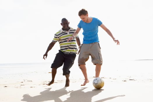 Two Young Men Palying Football On Beach Together