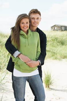 Romantic Young Couple Standing By Dunes With Beach Hut In Distance