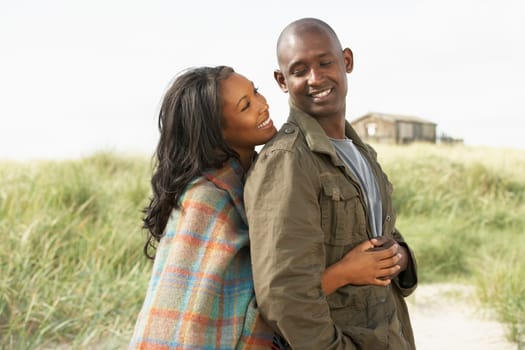 Romantic Young Couple Standing By Dunes With Beach Hut In Distance