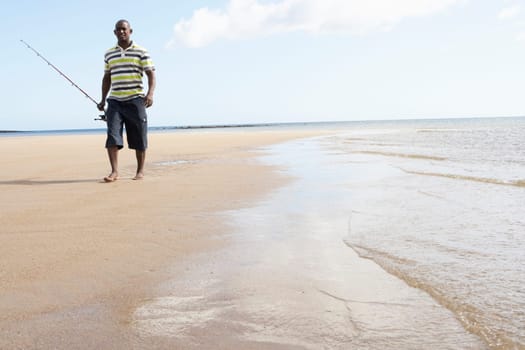 Man Walking Along Shore Of Beach Carrying Fishing Rod