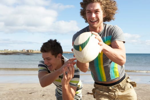 Two Teenage Boys Playing Rugby On Beach Together
