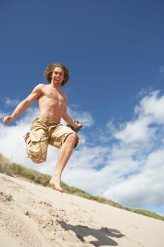 Young Man Running Down Sand Dune On Beach