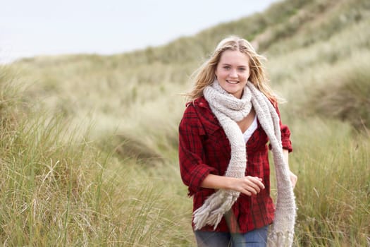 Teenage Girl Walking Through Sand Dunes Wearing Warm Clothing