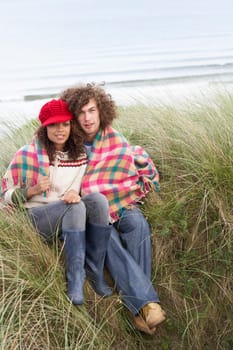 Young Couple Sitting In Sand Dunes Wrapped In Blanket