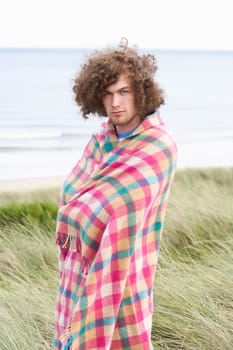 Young Man Standing In Sand Dunes Wrapped In Blanket