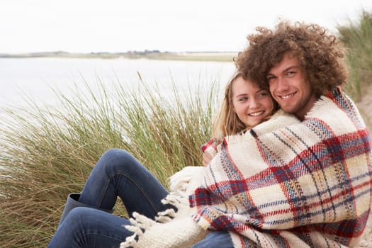 Teenage Couple Sitting In Sand Dunes Wrapped In Blanket