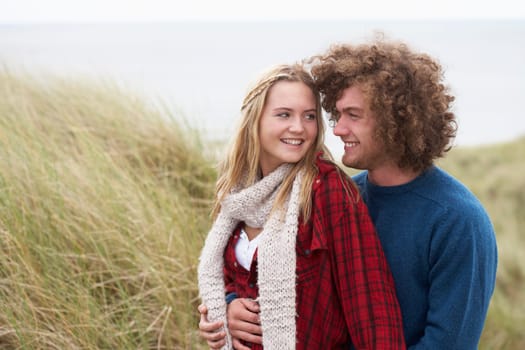 Teenage Couple Walking Through Sand Dunes Wearing Warm Clothing