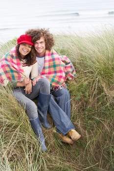 Young Couple Sitting In Sand Dunes Wrapped In Blanket