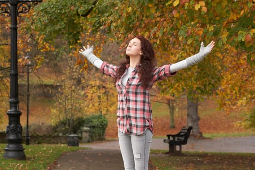Teenage Girl Standing In Autumn Park With Arms Outstretched