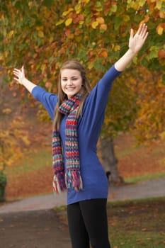 Teenage Girl Standing In Autumn Park With Arms Outstretched