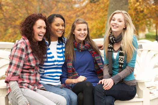 Group Of Four Teenage Girls Sitting On Bench In Autumn Park