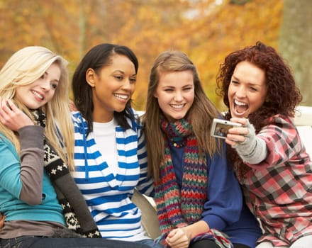 Group Of Four Teenage Girls Taking Picture With Camera Sitting On Bench In Autum