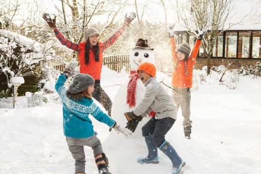 Mother And Children Building Snowman In Garden