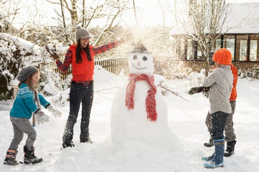 Mother And Children Building Snowman In Garden